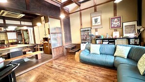 Una habitación tradicional japonesa con suelo de tatami, una mesa de madera baja, un sofá azul y una estantería con diversos objetos.