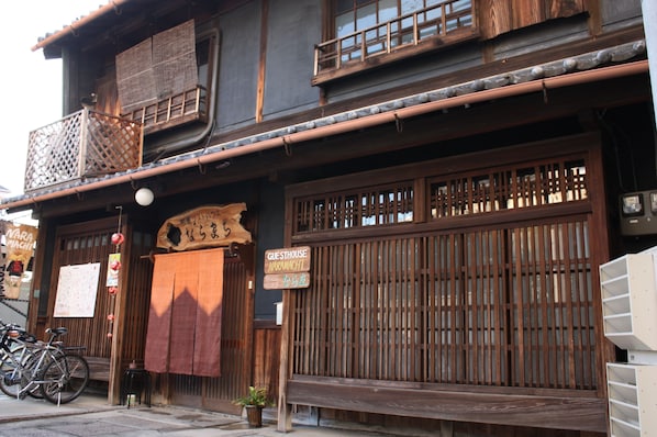 A traditional Japanese building with a wooden exterior, a sign indicating a guesthouse, and bicycles parked outside.