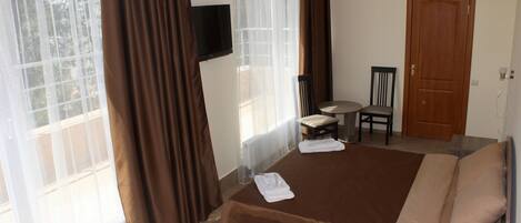 Una habitación de hotel con una cama, una silla, una mesita y un televisor colocado en la pared.