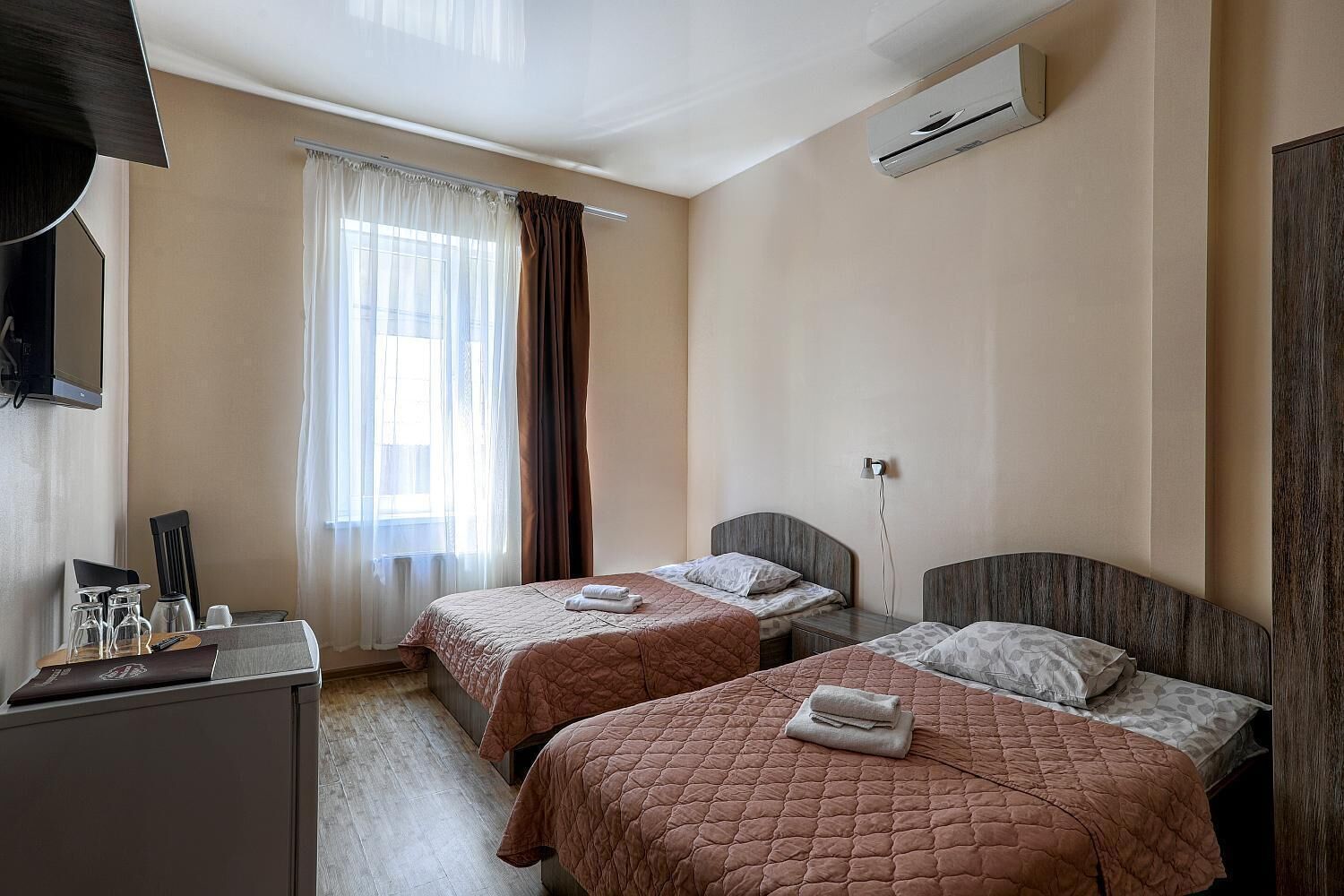 Habitación de hotel con dos camas, un escritorio, un televisor y un aire acondicionado.