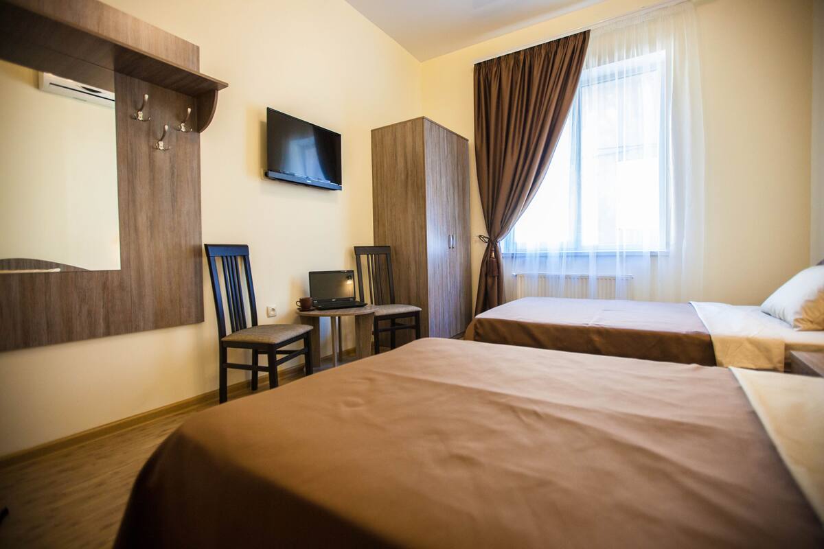 A hotel room with two beds, a desk with a computer, a television, and a wardrobe.
