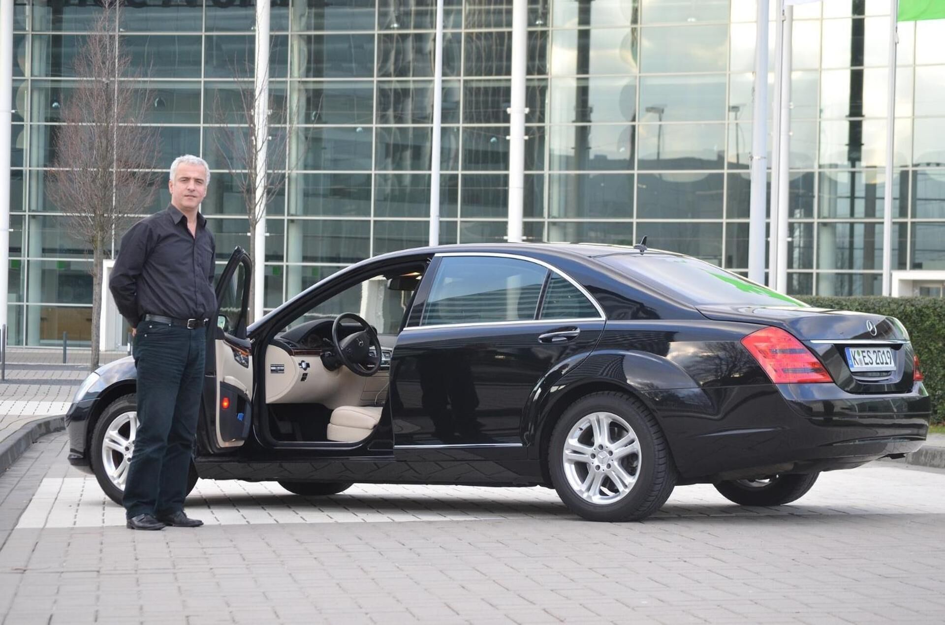 A black car parked in front of a modern building with glass windows.