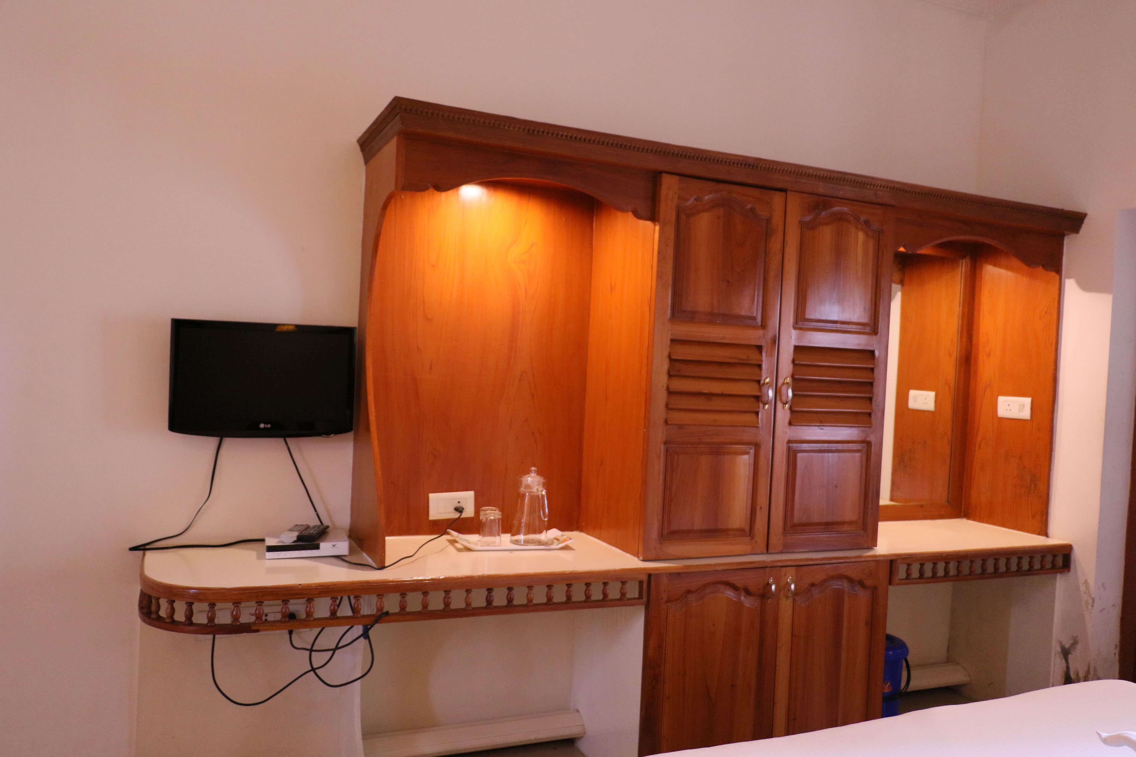 Una habitación con un armario de madera, un televisor de pantalla plana montado en la pared y una pequeña mesa con un control remoto.