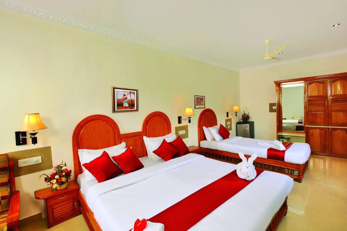 Habitación de hotel con dos camas, cabeceros de madera, ropa de cama blanca, almohadas rojas, un tapete rojo, una decoración de conejo blanco, una mesita de noche con una lámpara, un jarrón de flores y un mueble de tocador con espejo.