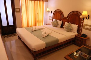Habitación de hotel con una cama grande, dos almohadas, una mesita de noche con lámpara y una pequeña mesa con un libro.
