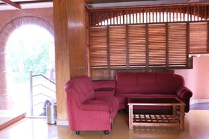 A red sofa, a wooden coffee table, and a window with blinds in a room with a tiled floor.