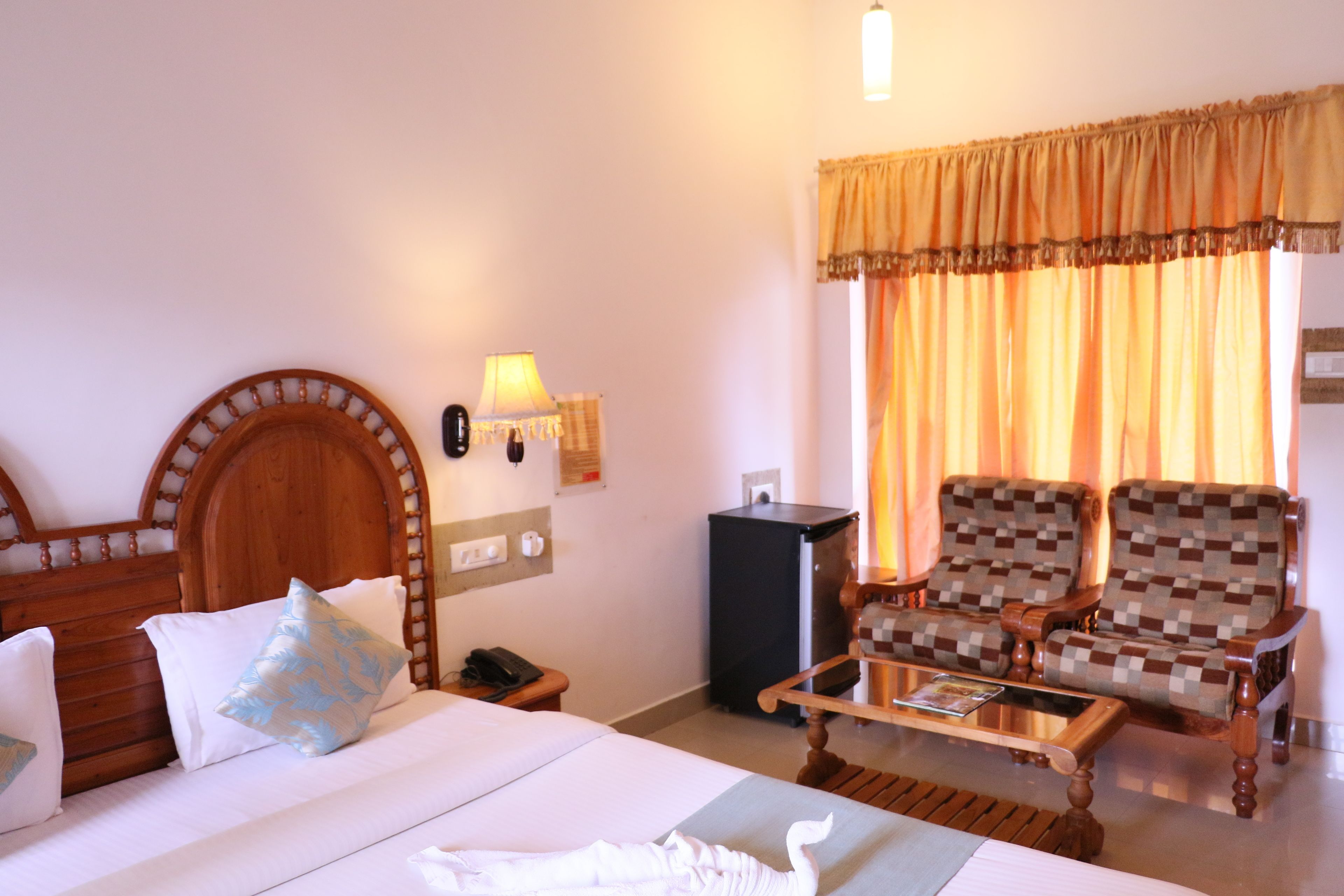 A hotel room with a wooden bed, two armchairs, a small table, a lamp, and a window with curtains.