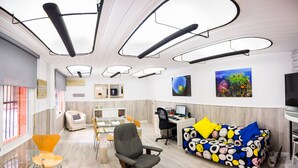 A modern office space with a glass table, office chairs, a desk with a computer, a colorful sofa, and artwork on the walls. - Hostal Guillot (Torremolinos)