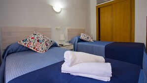 A hotel room with two beds, each with a blue bedspread and decorative pillows. There is a stack of white towels on the floor. - Hostal Guillot (Torremolinos)