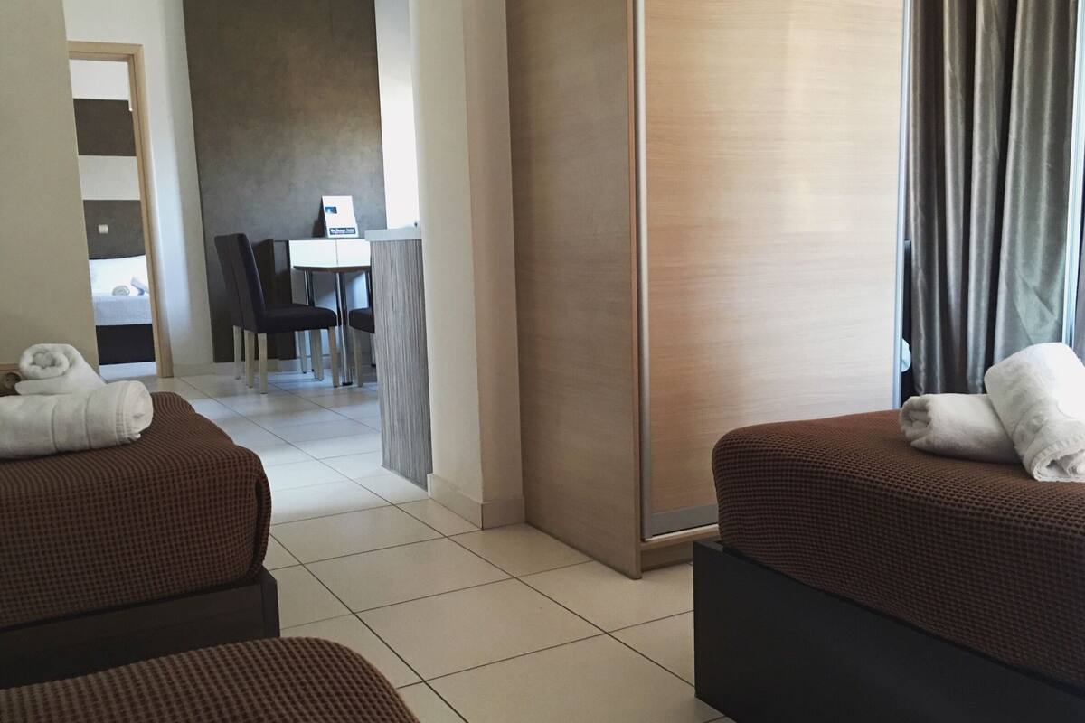 A hotel room with two brown upholstered sofas, a wooden sideboard, and a view of the dining area.