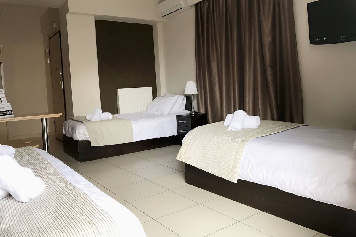 A hotel room with two beds, a desk, a chair, a lamp, and a TV.