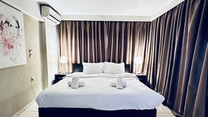 A modern hotel room with a large bed, a ceiling fan, and a view of the city through the window.