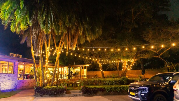 A nighttime outdoor area with string lights, palm trees, and a parked SUV. - Casa Mia (Blantyre)