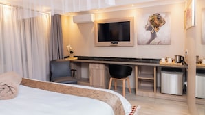 A modern hotel room with a bed, a desk, a chair, a TV, and a small kitchenette. - Casa Mia (Blantyre)