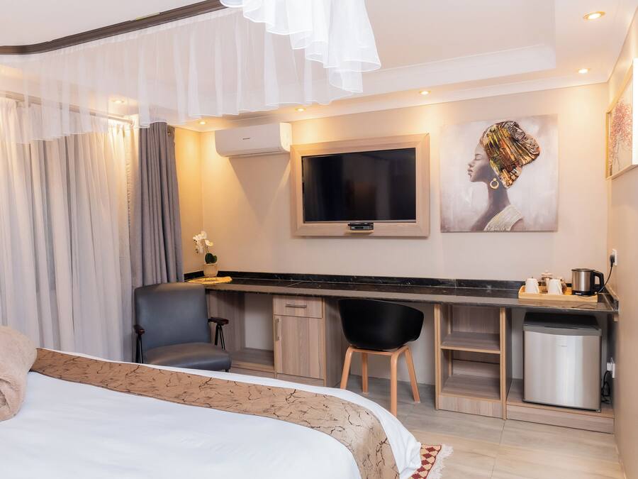 A modern hotel room with a bed, a desk, a chair, a TV, and a small kitchenette.
