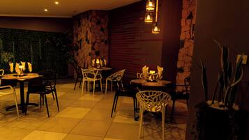 Un comedor con mesas y sillas, un muro de piedra y luces colgantes.