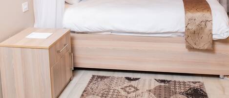A bedroom with a bed, a bedside table, a nightstand, and a patterned rug.