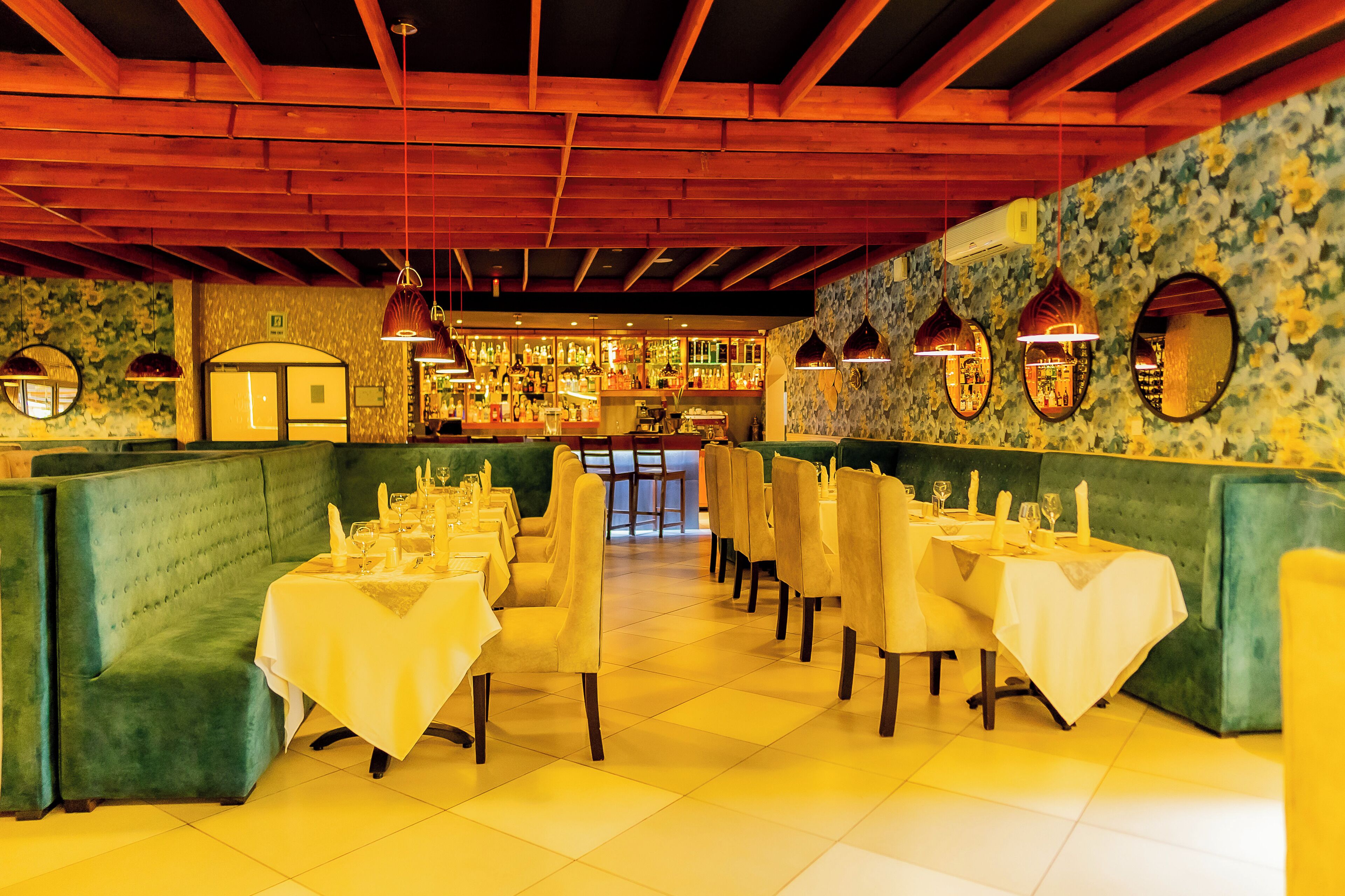 A restaurant with booths and tables, wooden beams on the ceiling, and a bar area in the background.