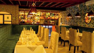 Un restaurante con una larga mesa de comedor dispuesta para una comida, asientos acolchados y una zona de bar al fondo.