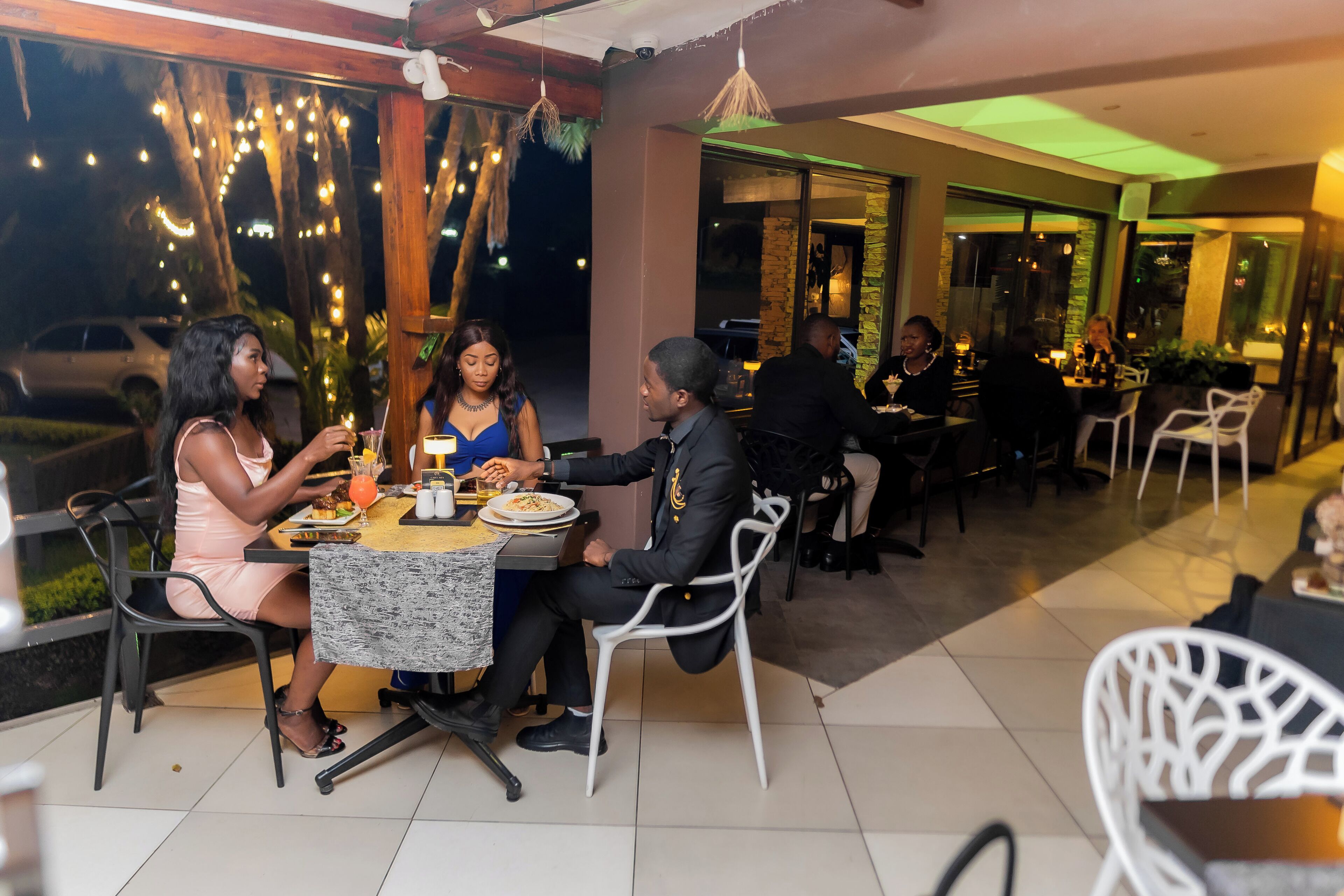 An outdoor dining area with tables and chairs, string lights, and a view of the street.