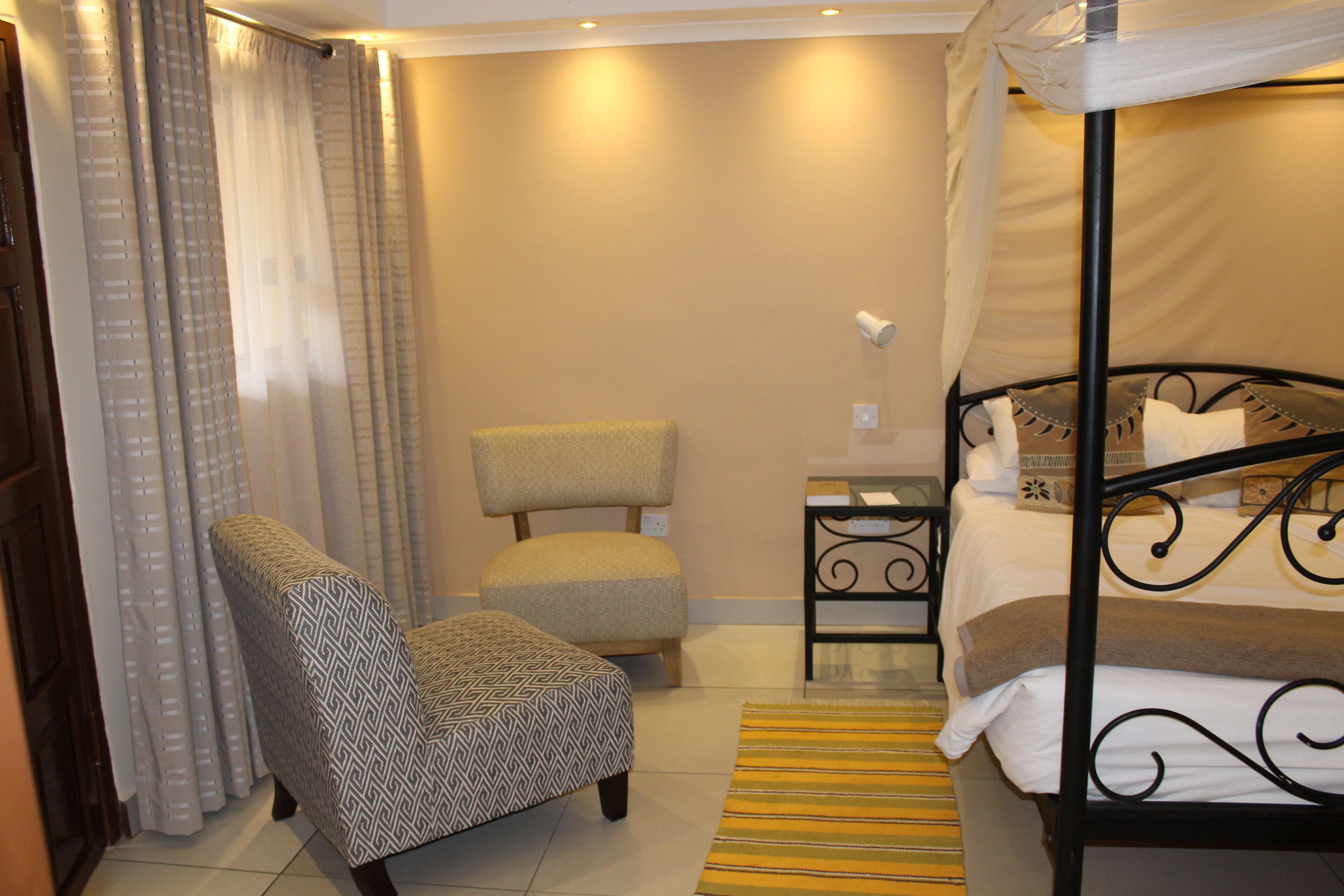 A hotel room with a bed, a chair, a nightstand, and curtains.