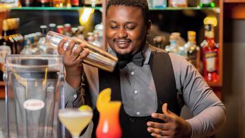 A bartender preparing a drink behind a bar with various bottles and a cocktail shaker.