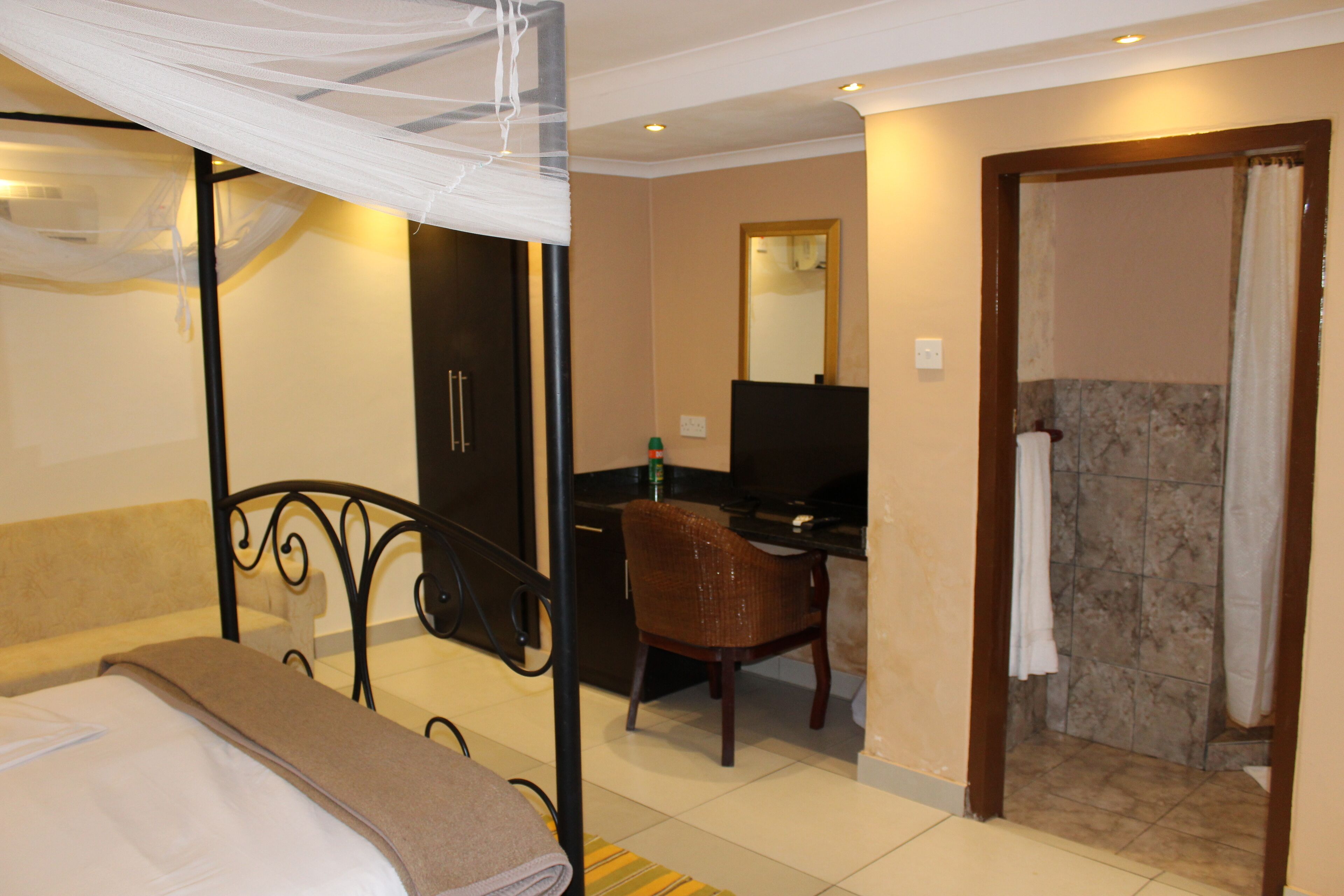 A hotel room with a bed, a desk, a chair, a mirror, and a shower area.