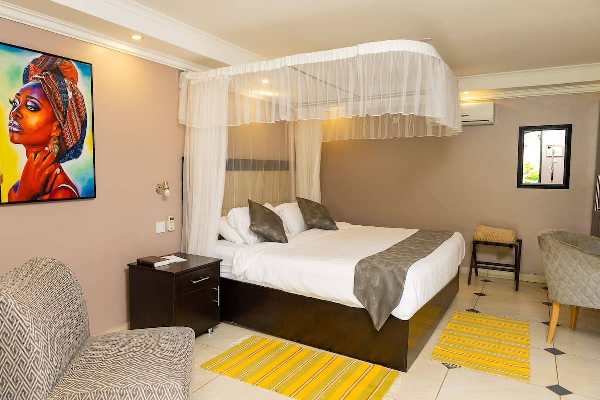 A bedroom with a bed, bedside table, chair, and artwork on the wall.