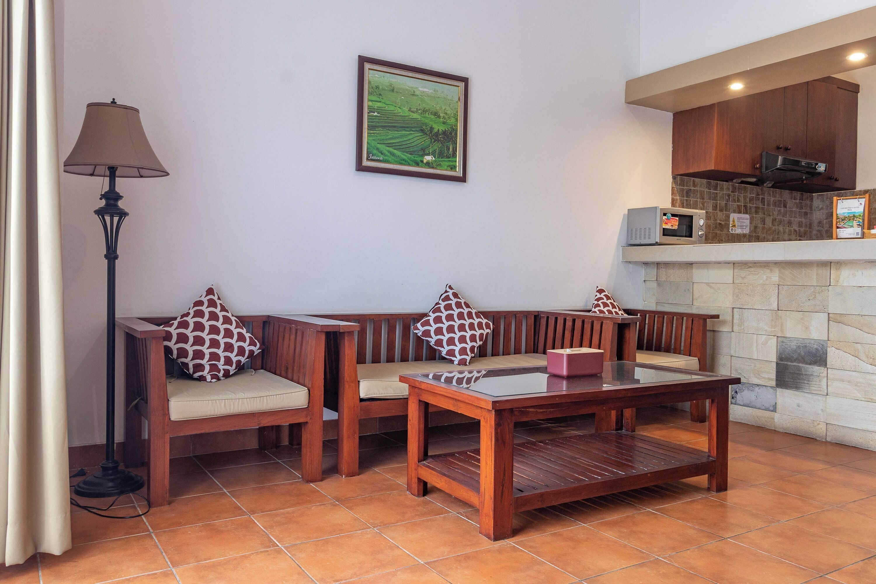 A seating area with a wooden bench and a table, a lamp, a framed picture on the wall, and a kitchen area with a microwave.