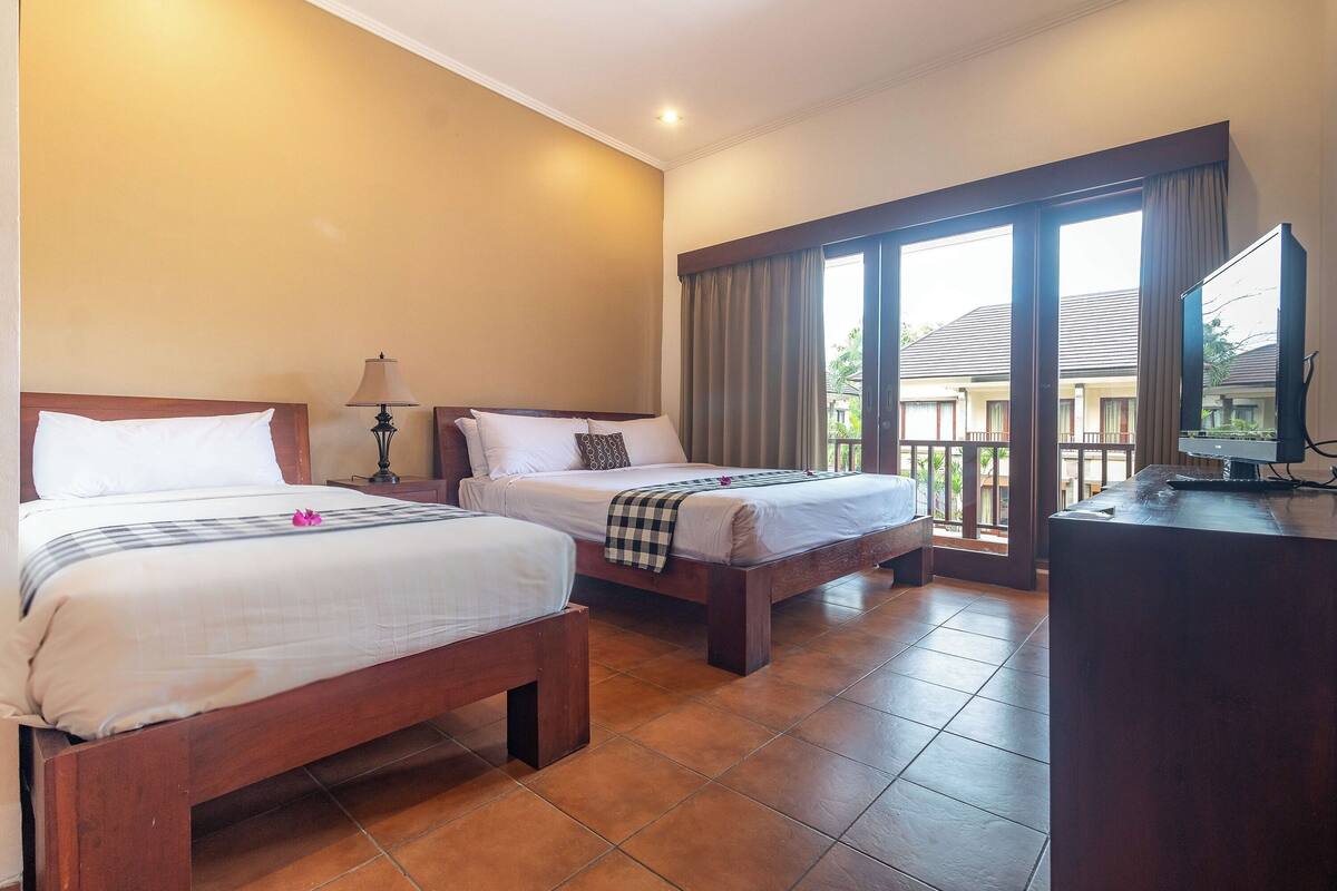 Una habitación de hotel con dos camas de madera, un escritorio con televisión y un ventanal con cortinas.