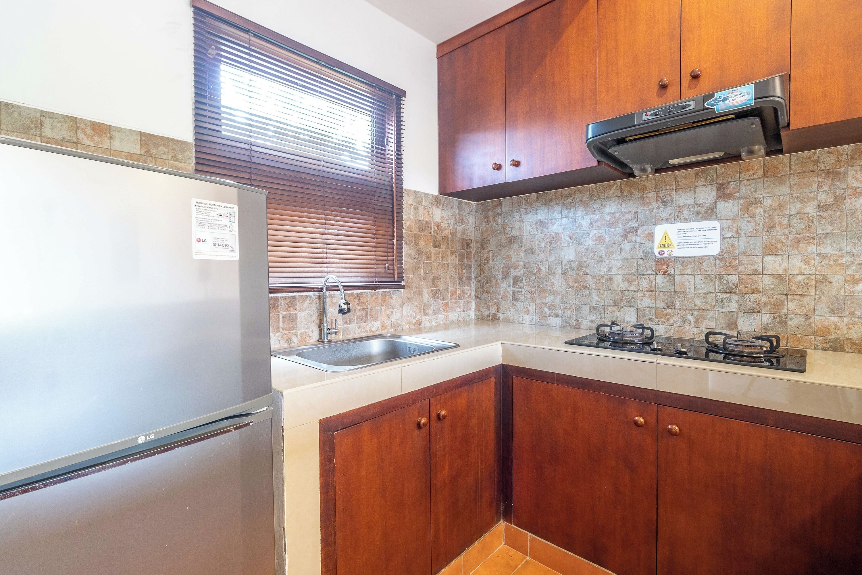 A kitchen with wooden cabinets, a stainless steel refrigerator, a gas stove, and a window with blinds.
