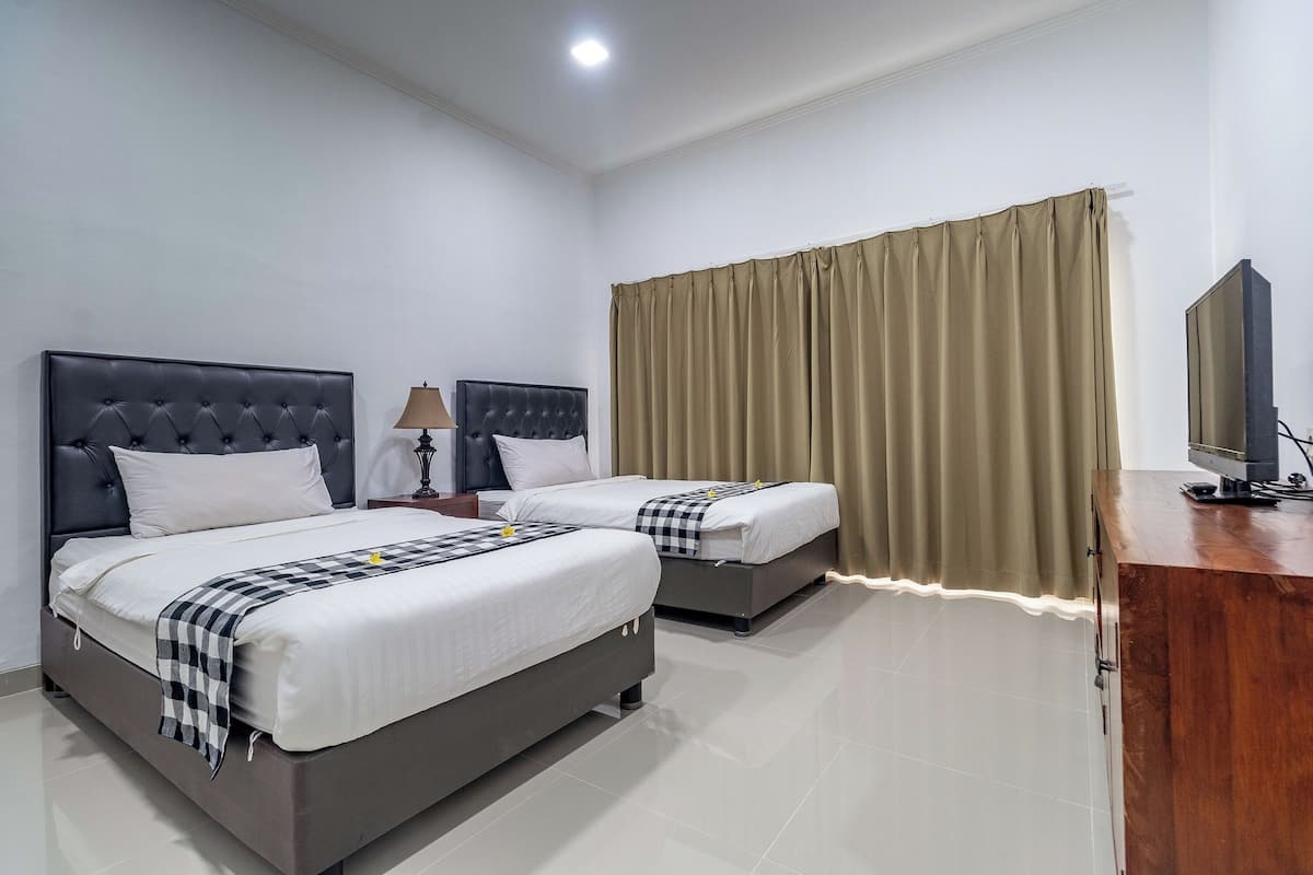 Habitación de hotel con dos camas, un escritorio, una lámpara y un televisor.