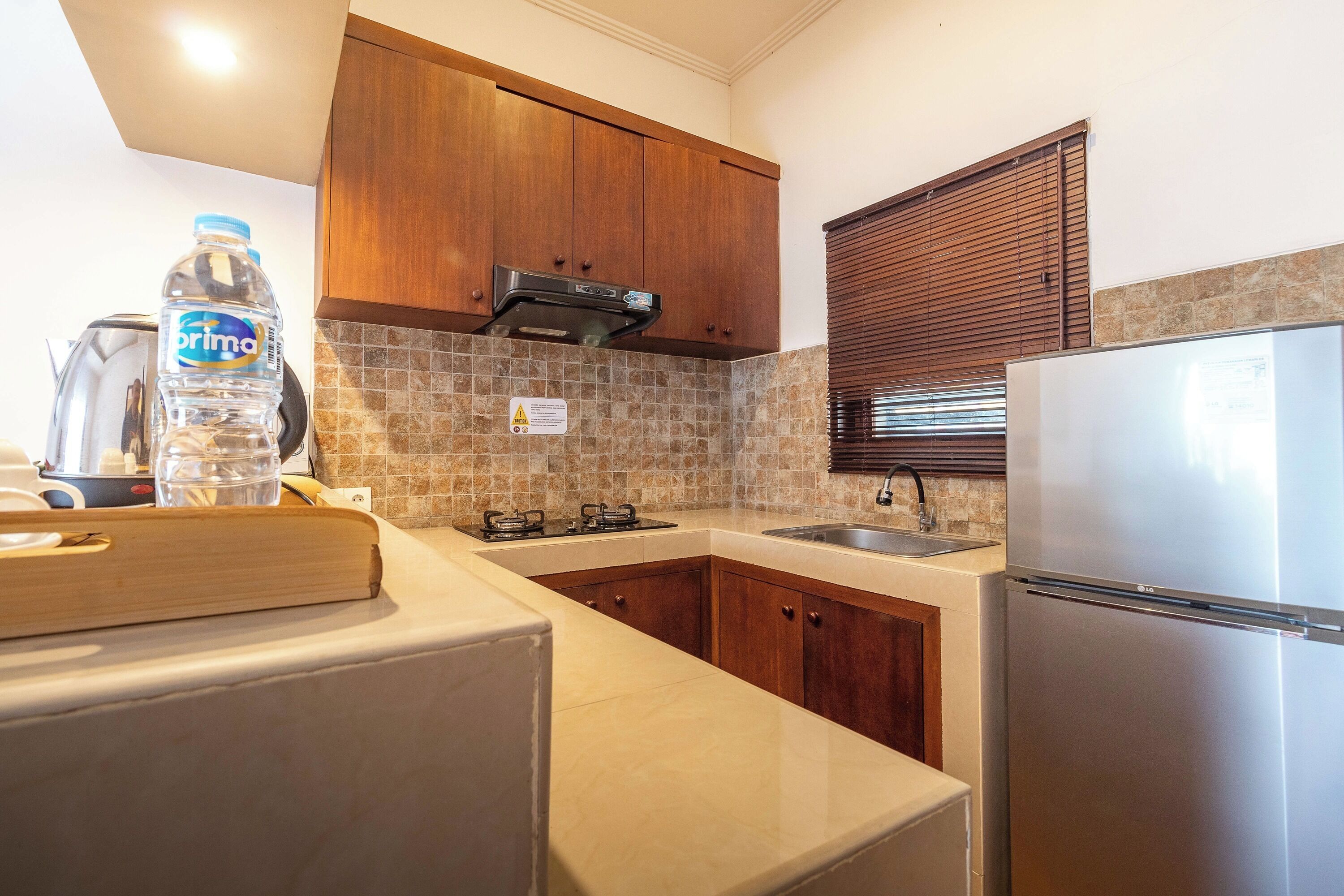 A kitchen with wooden cabinets, a stainless steel refrigerator, a gas stove, and a tiled backsplash.