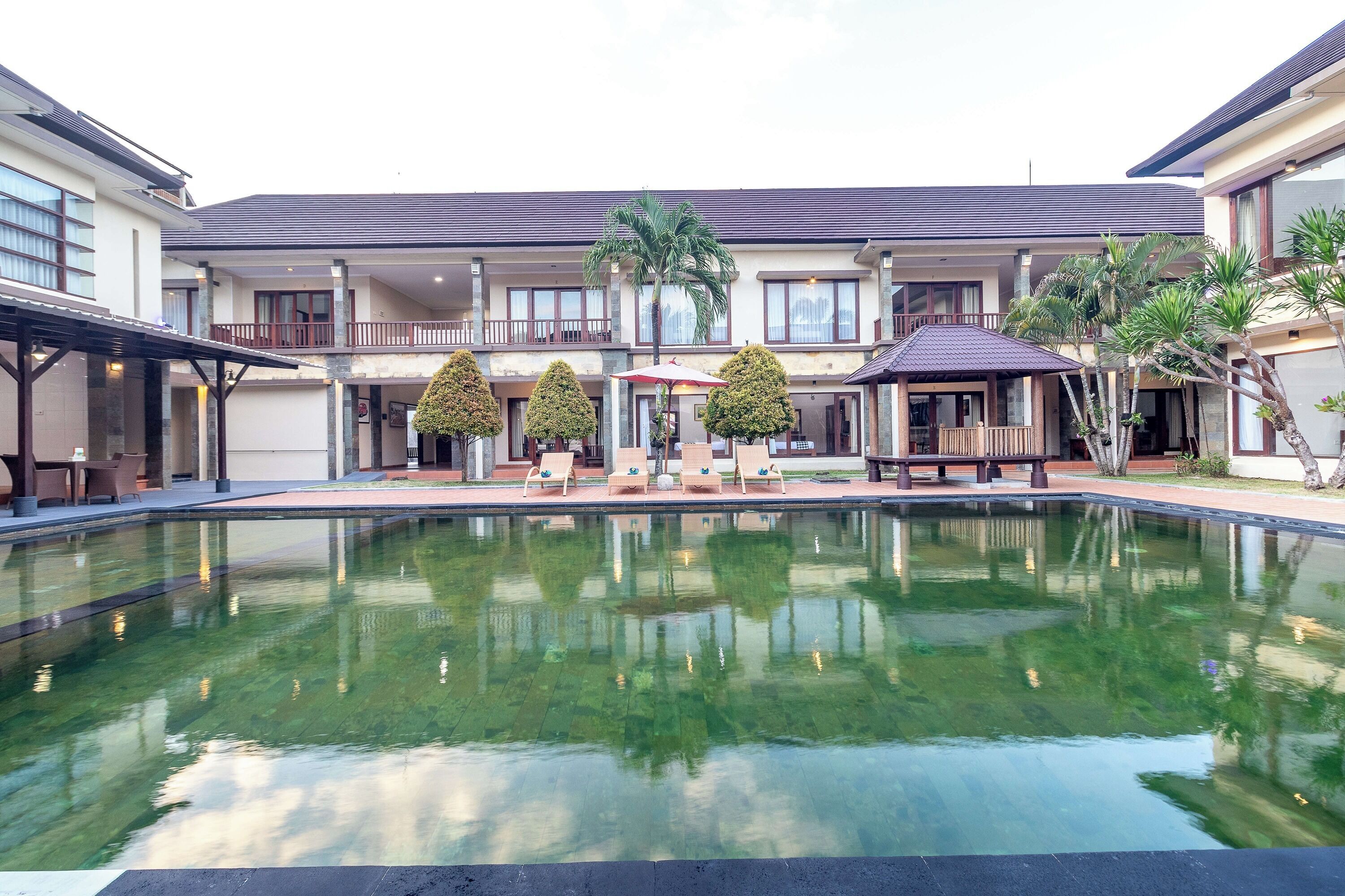 A hotel courtyard with a swimming pool, lounge chairs, and palm trees.