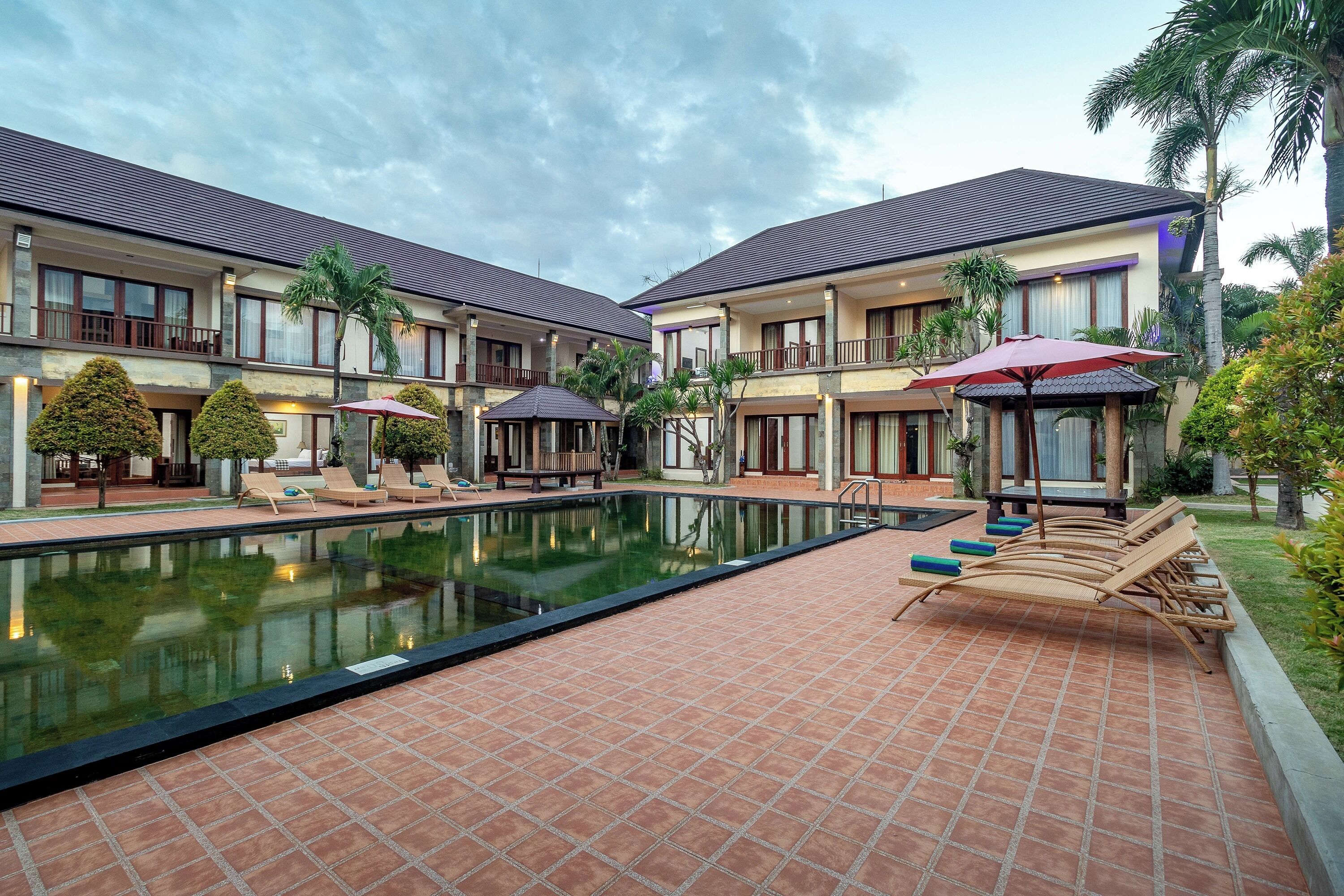 A hotel with a swimming pool, lounge chairs, and palm trees.