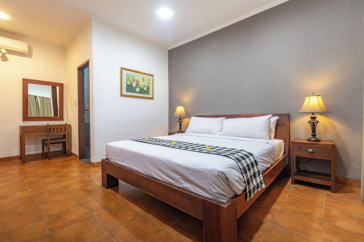 Un dormitorio con una cama de madera, dos mesitas de noche con lámparas, un escritorio pequeño, una silla y un cuadro en la pared.