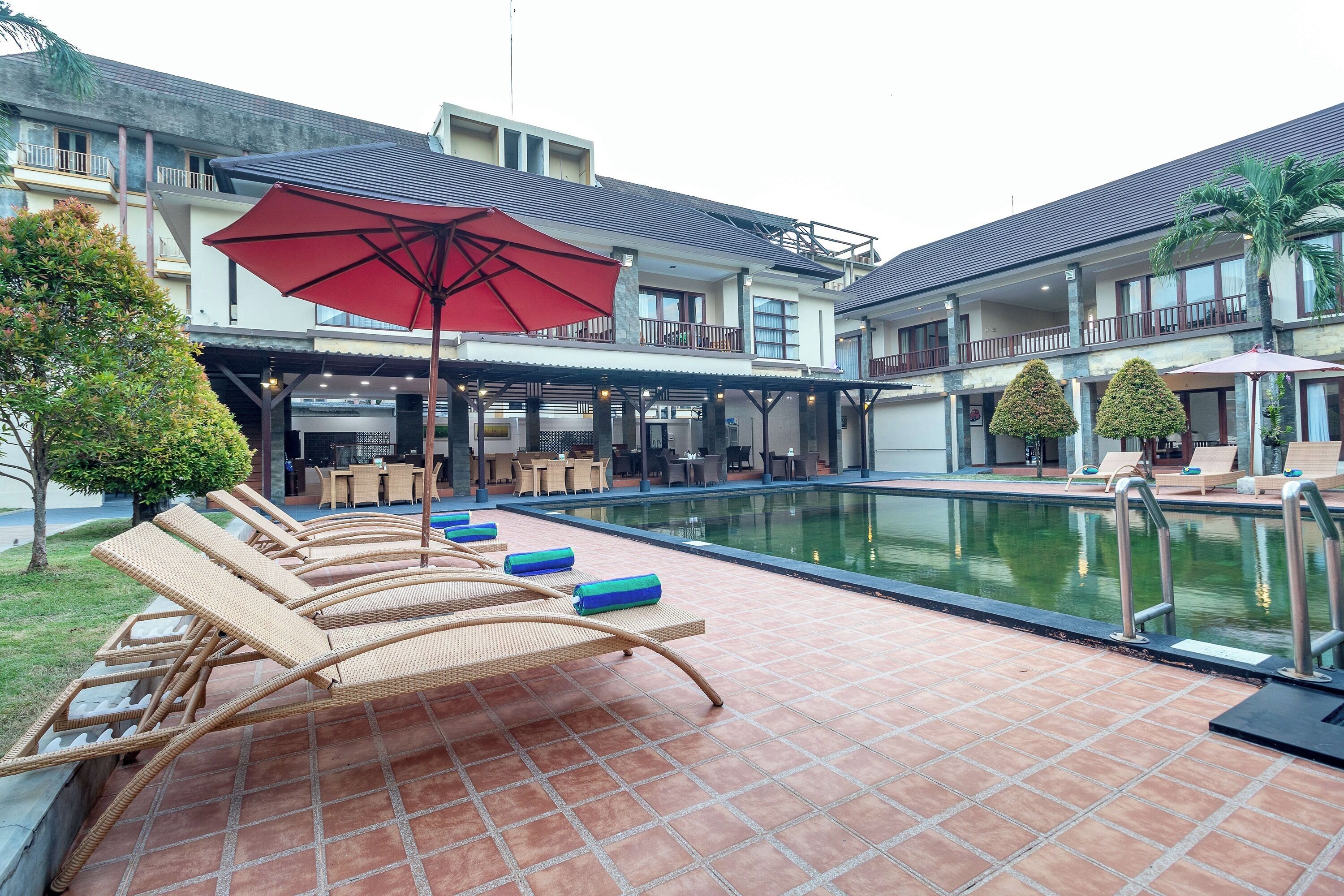A poolside area with lounge chairs and umbrellas, a pool, and a building with balconies and outdoor seating.
