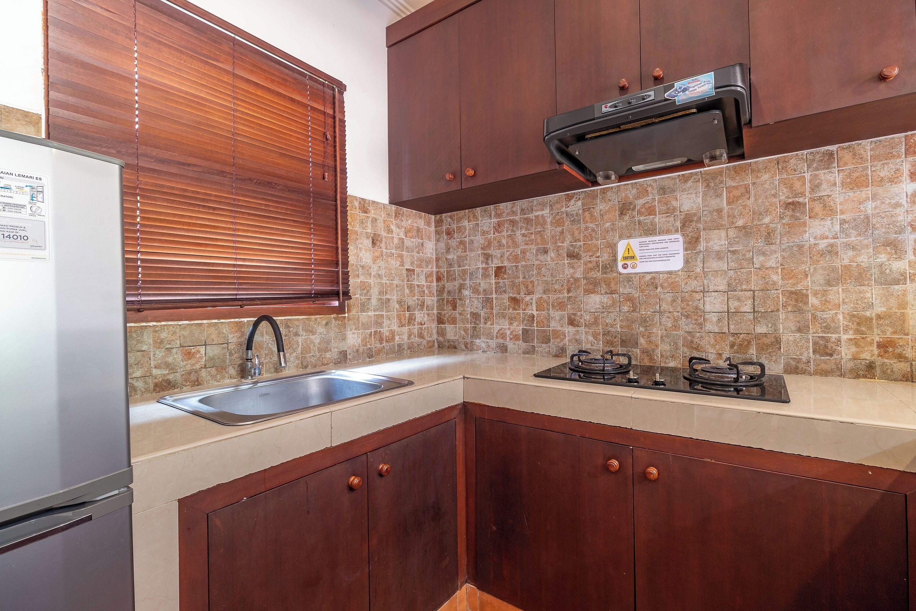 Une cuisine avec des meubles en bois, un évier en acier inoxydable, une cuisinière encastrée et une fenêtre avec des stores.