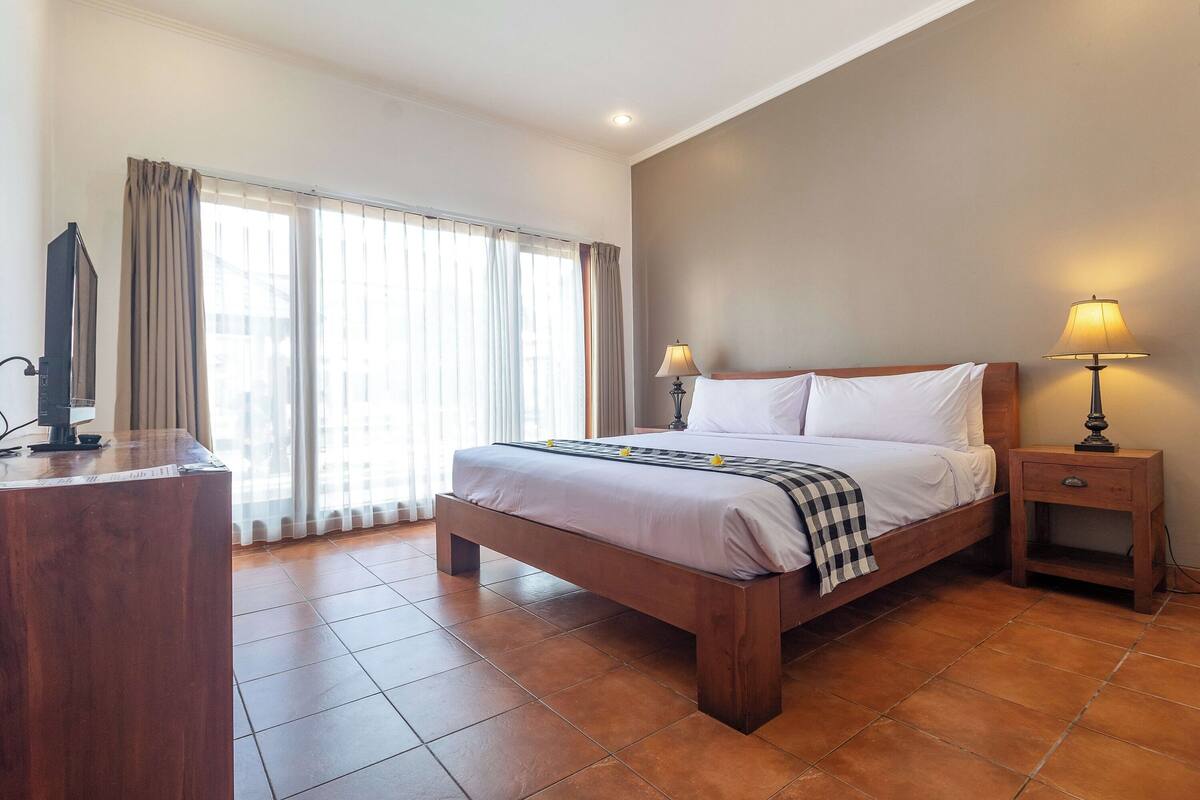 Una habitación de hotel con cama, mesitas de noche, un escritorio y una ventana con cortinas.