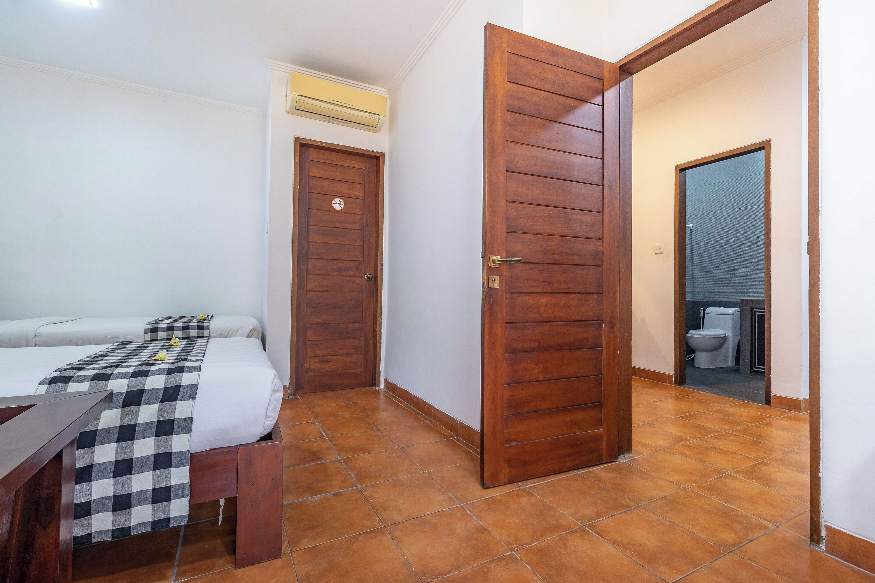A hotel room with a bed, a checkered blanket, a wooden door, and a bathroom visible through an open door.