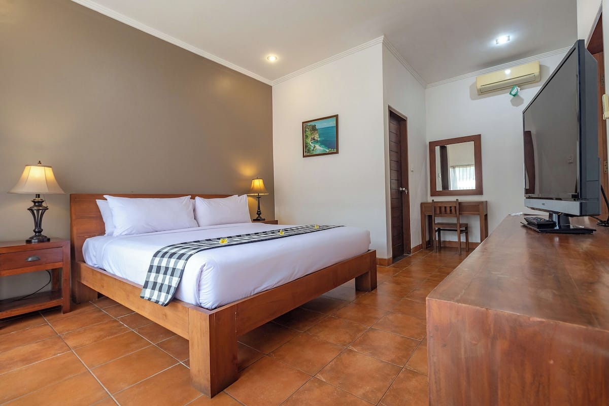 Habitación de hotel con cama de madera, escritorio, silla, televisión y aire acondicionado.