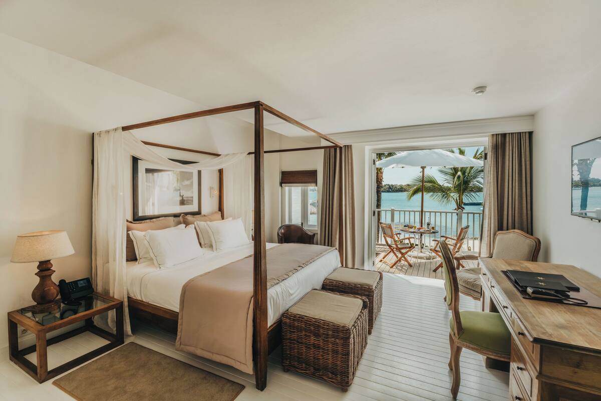 A four-poster bed with a view of the ocean, a desk with a chair, and a small table with a lamp.