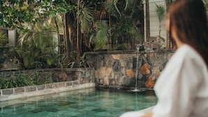 Una piscina de agua cristalina, rodeada de muros de piedra y plantas tropicales.