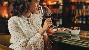Una persona sentada en la barra, con una copa de vino, un bol de comida y una botella de vino sobre la encimera.
