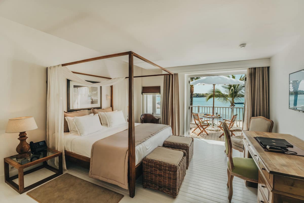 A four-poster bed with a view of the ocean, a desk with a chair, and a small table with a lamp.