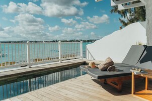 Zona de piscina con sillas de descanso y una terraza de madera con vista a un cuerpo de agua.