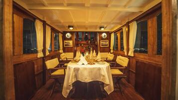 Un comedor con paredes de madera, una mesa preparada para cuatro personas con manteles blancos y cuadros en las paredes.
