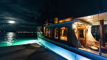 Un barco con zona de comedor cubierta y vista al océano de noche.