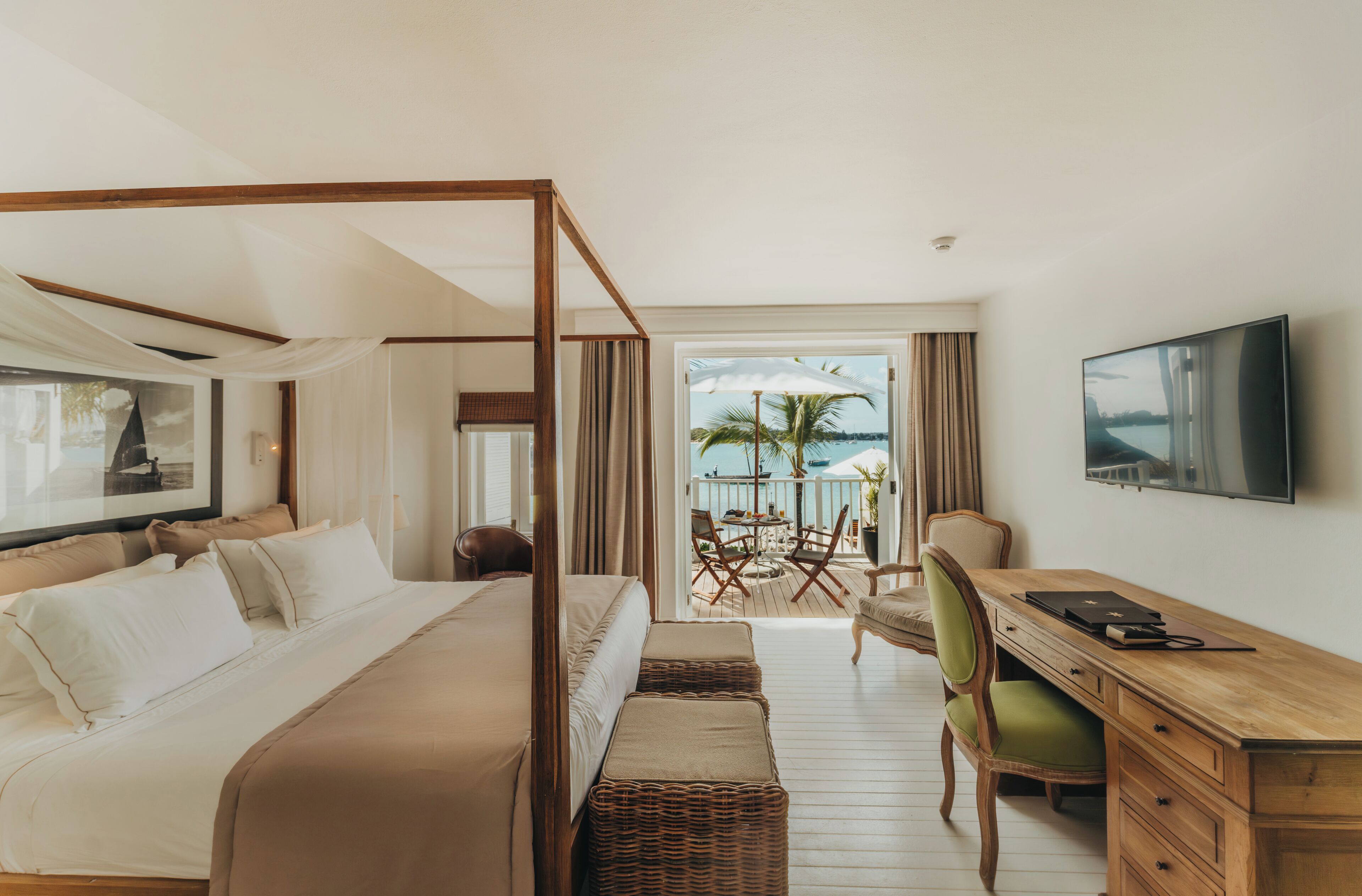 A bedroom with a four-poster bed, a desk, a chair, and a television.