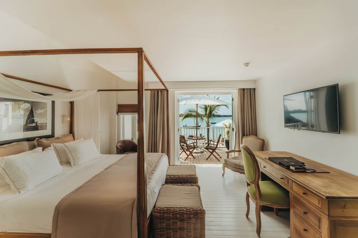 A spacious bedroom with a four-poster bed, a wooden desk, and a television.